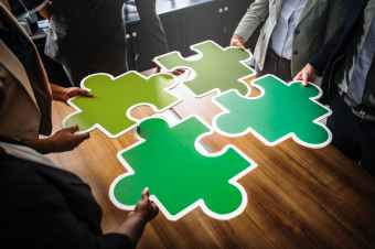 four people holding four jigsaw pieces on top of brown wooden table
